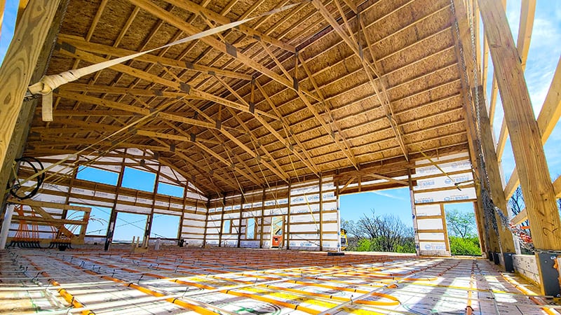 Open interior framing of the Cedar barndominium during construction, showing the wide clear span of the post-frame structure
